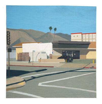 view of san gabriel blvd location showing asphalt street and sidewalk and parking lot in the foreground and a building in the mid-ground and mountains in the background bare from the Eaton Fire. The sun casts long shadows from the street lamp and traffic signal onto the pavement.